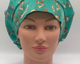 May include: A teal surgical scrub cap with a repeating pattern of cartoon cats dressed as surgeons. The cats wear surgical masks and scrubs, holding medical instruments. The cap is displayed on a mannequin head.