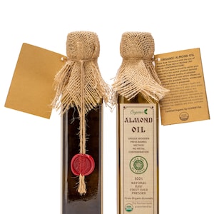 May include: Two glass bottles of organic almond oil with burlap coverings and red wax seals. The bottles are labelled with the words "Organic Almond Oil" and "Live Oil by Lesna".