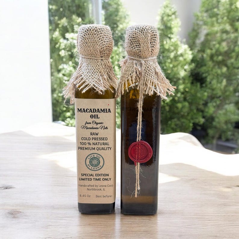 May include: Two bottles of macadamia oil with burlap and twine accents. Each bottle has a label with text that reads "Macadamia Oil" and "Raw Cold Pressed 100% Natural Premium Quality". One bottle has a red wax seal.
