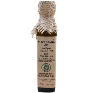 May include: A slender glass bottle of macadamia oil. The label reads "MACADAMIA OIL" and details about the product, including "RAW COLD PRESSED 100% NATURAL PREMIUM QUALITY." The bottle is topped with a burlap fabric. The bottle contains 8.45 oz of oil.