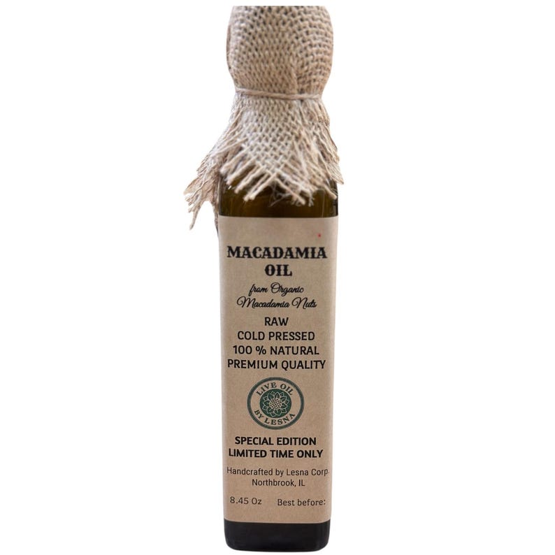 May include: A slender glass bottle of macadamia oil. The label reads "MACADAMIA OIL" and details about the product, including "RAW COLD PRESSED 100% NATURAL PREMIUM QUALITY." The bottle is topped with a burlap fabric. The bottle contains 8.45 oz of oil.