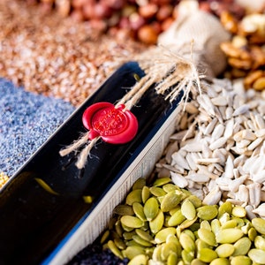 Peut inclure: Une bouteille en verre fonc&eacute; avec un sceau de cire rouge et de la ficelle attach&eacute;e autour du cou. La bouteille est entour&eacute;e de diverses graines et noix, notamment des graines de tournesol, des graines de citrouille, des graines de pavot, des graines de lin et des noix.