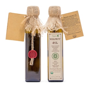 May include: Two glass bottles of organic walnut oil with burlap coverings and red wax seals. The bottles are labeled with the words "Organic Walnut Oil" and "Live Oil by Lesna". The bottles are 8.45 oz (250 ml).