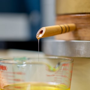 Peut inclure: Un bec en bois avec une goutte de liquide dor&eacute; se versant dans une tasse &agrave; mesurer en verre transparente.