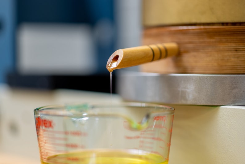 Peut inclure: Un bec en bois avec une goutte de liquide dor&eacute; se versant dans une tasse &agrave; mesurer en verre transparente.