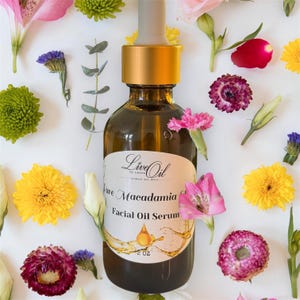 May include: A brown glass bottle of "Pure Macadamia Facial Oil Serum" with a gold cap and dropper, surrounded by colorful flowers. The label reads "Live Oil" and the bottle contains 2 fl oz of product.