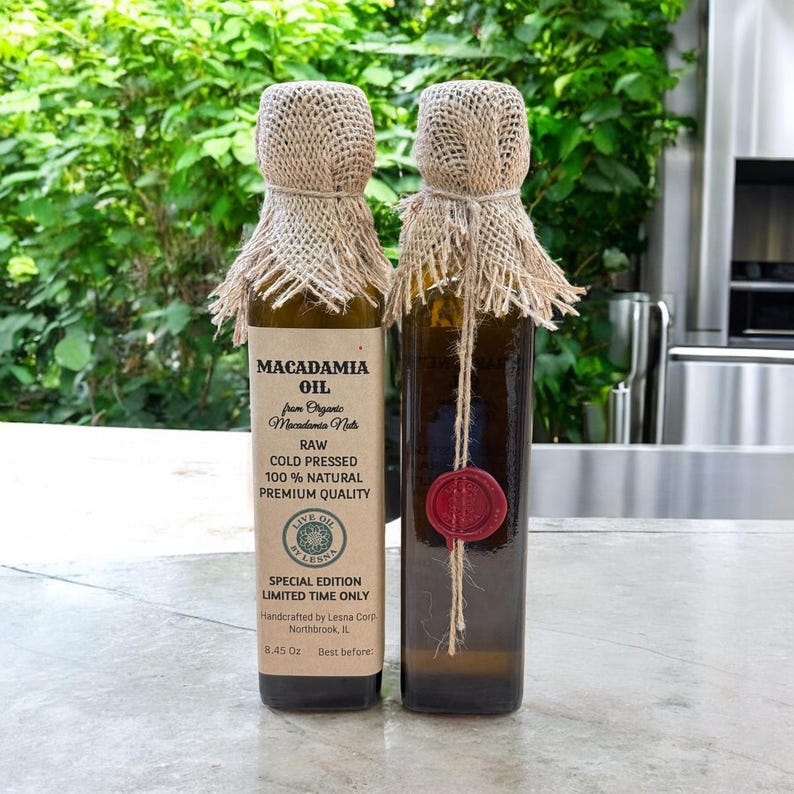 May include: Two bottles of macadamia oil with burlap and twine accents. The labels read "Macadamia Oil" and detail the product's raw, cold-pressed, and natural qualities. One bottle has a red wax seal.