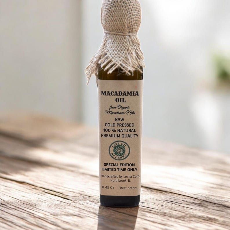 May include: A glass bottle of macadamia oil with a burlap cover on the top. The label reads "MACADAMIA OIL" and "RAW COLD PRESSED 100% NATURAL PREMIUM QUALITY." The bottle contains 8.45 oz of oil.