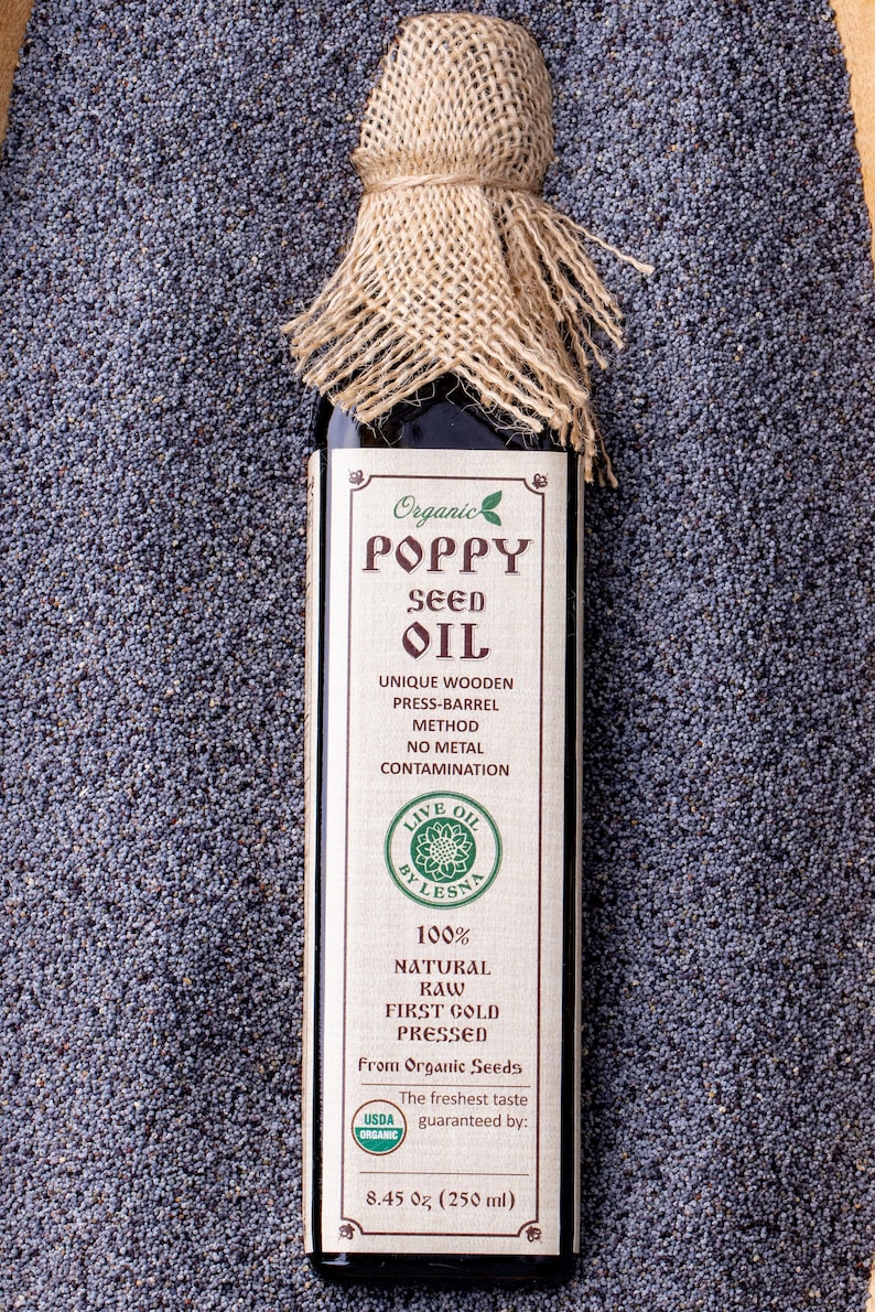 May include: A glass bottle of organic poppy seed oil with a burlap covering. The label reads "Organic Poppy Seed Oil", "Unique Wooden Press-Barrel Method", "No Metal Contamination", "Live Oil by Lesna", "100% Natural Raw First Cold Pressed", "From Organic Seeds", "USDA Organic", "The freshest taste guaranteed by:", "8.45 oz (250 ml)".