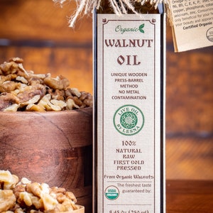 May include: A glass bottle of organic walnut oil with a brown label. The label says "Organic Walnut Oil", "Unique Wooden Press-Barrel Method", "No Metal Contamination", "Live Oil by Lesna", "100% Natural Raw First Cold Pressed", "From Organic Walnuts", "The freshest taste guaranteed by:", and "8.45 oz (250 ml)". There is a USDA Organic seal on the label. The bottle is sitting on a wooden surface next to a bowl of walnuts.