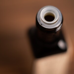 May include: Close-up of the top of a dark glass bottle with a white plastic cap. The cap has a small hole in the centre.