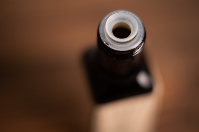 May include: Close-up of the top of a dark glass bottle with a white plastic cap. The cap has a small hole in the centre.