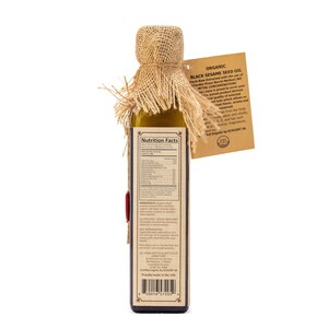 May include: A glass bottle of organic black sesame seed oil with a burlap covering. The bottle has a label with nutrition facts and ingredients. The label also states that the oil is certified organic by ECOCERT SA and proudly made in the USA.