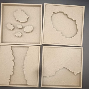 Könnte beinhalten: Vier beige quadratische Tabletts mit erhöhten Kanten. Jedes Tablett weist ein einzigartiges Ausschnittdesign auf, das abstrakten Landformationen ähnelt. Die Ausschnitte variieren in Form und Größe und erzeugen eine strukturierte, künstlerische Darstellung. Die Tabletts sind in einem Raster angeordnet.