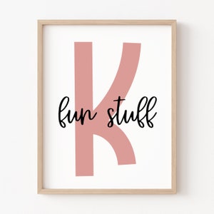 May include: A framed print featuring a pink letter K and the text "fun stuff" in black cursive writing.