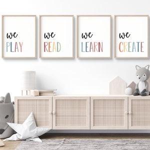 Könnte beinhalten: Vier gerahmte Drucke mit den Worten "We Play", "We Read", "We Learn" und "We Create" in bunten Schriftzügen auf weißem Hintergrund. Die Drucke hängen an einer weißen Wand über einem Holzschrank.