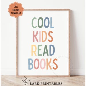 May include: A framed print with the words "COOL KIDS READ BOOKS" in colorful, playful lettering. The text is arranged vertically on a white background, with a light brown frame. A digital download icon is in the upper left corner.