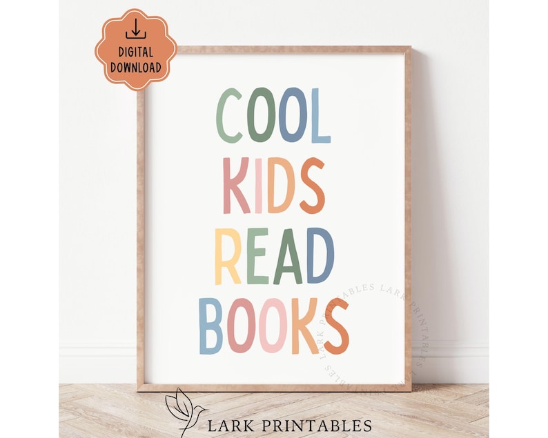 May include: A framed print with the words "COOL KIDS READ BOOKS" in colorful, playful lettering. The text is arranged vertically on a white background, with a light brown frame. A digital download icon is in the upper left corner.