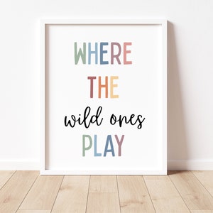 May include: A white framed print with the text "WHERE THE wild ones PLAY" in colorful letters. The words "WHERE" and "PLAY" are in a rainbow of colors, while "THE" is in a light orange color.