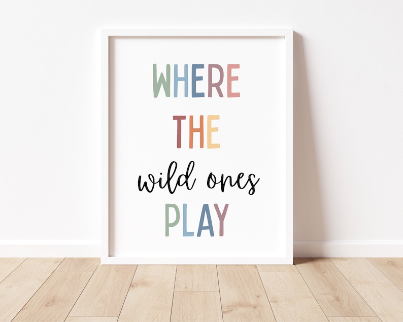 May include: A white framed print with the text "WHERE THE wild ones PLAY" in colorful letters. The words "WHERE" and "PLAY" are in a rainbow of colors, while "THE" is in a light orange color.
