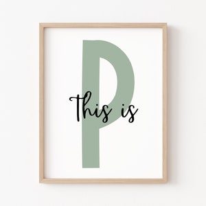 May include: A framed print with a large, sage green letter "P" and the text "This is" in black cursive font.