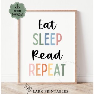 May include: A framed print with the words "Eat SLEEP Read REPEAT" in black, green, pink, blue, orange, and yellow. The print has a light brown frame and a digital download icon in the upper left corner.