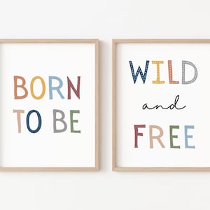 以下が含まれることがあります： カラフルなテキストが書かれた額装されたプリントが2枚。最初のプリントには「BORN TO BE」と虹色の文字で書かれています。2枚目のプリントには「WILD and FREE」と虹色の文字で書かれています。