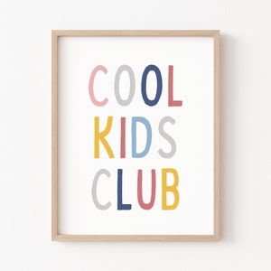 May include: A framed print with the text "COOL KIDS CLUB" in colorful, handwritten letters. The letters are in shades of pink, blue, yellow, and gray.
