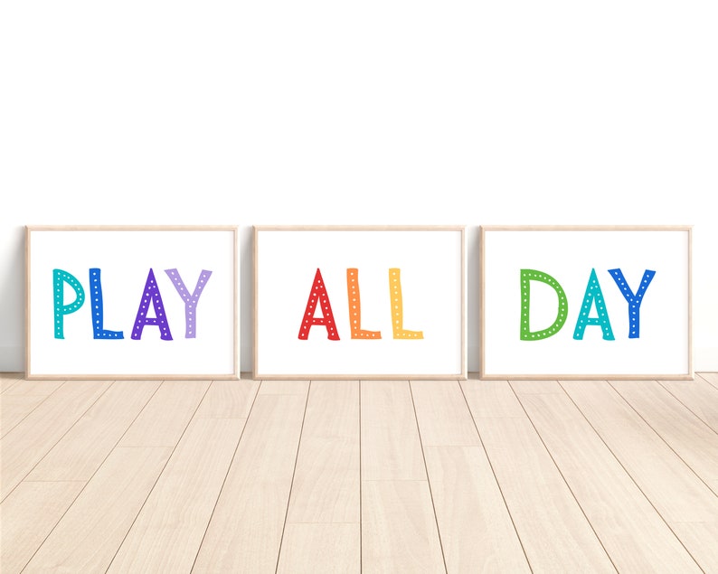 May include: Three framed prints with the words "PLAY ALL DAY" in colorful, whimsical lettering. Each word is in a different color, with a dotted pattern. The frames are a light wood color, and the background is white.