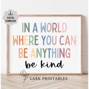 May include: A framed print with the text "IN A WORLD WHERE YOU CAN BE ANYTHING be kind" in various pastel colors. The print is a digital download and features the Lark Printables logo.