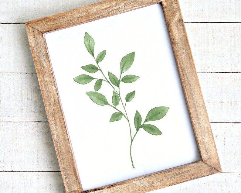 May include: A framed print of a watercolor painting of a green leafy branch with a white background.