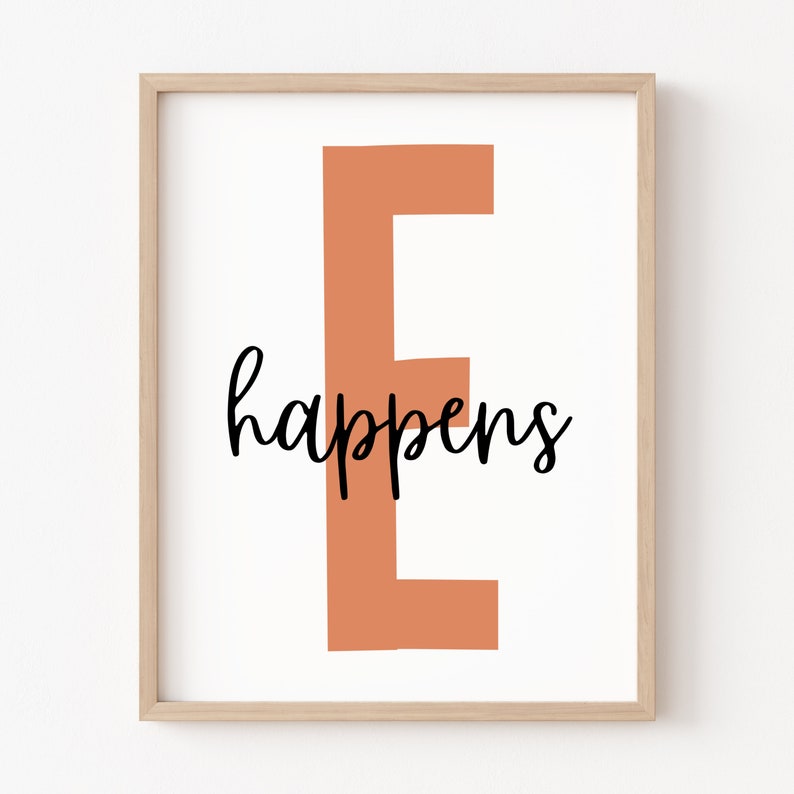 May include: A framed print featuring a peach-coloured letter "E" with the word "happens" written in black cursive underneath.