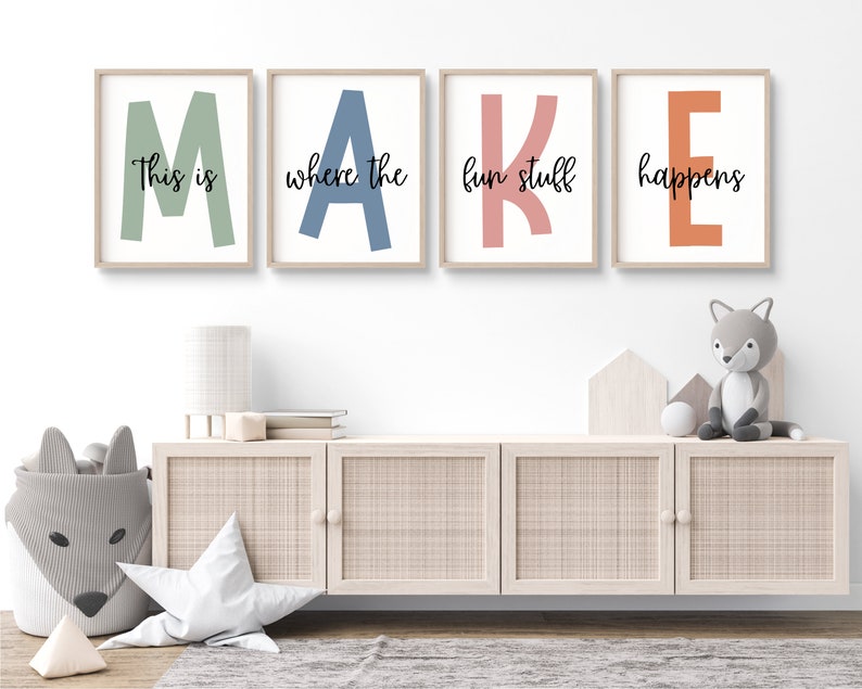 May include: Four framed prints spelling out the word "MAKE" in large, colourful letters. Each letter is a different colour: green, blue, pink, and orange. The text "This is where the fun stuff happens" is written in black cursive below the letters.