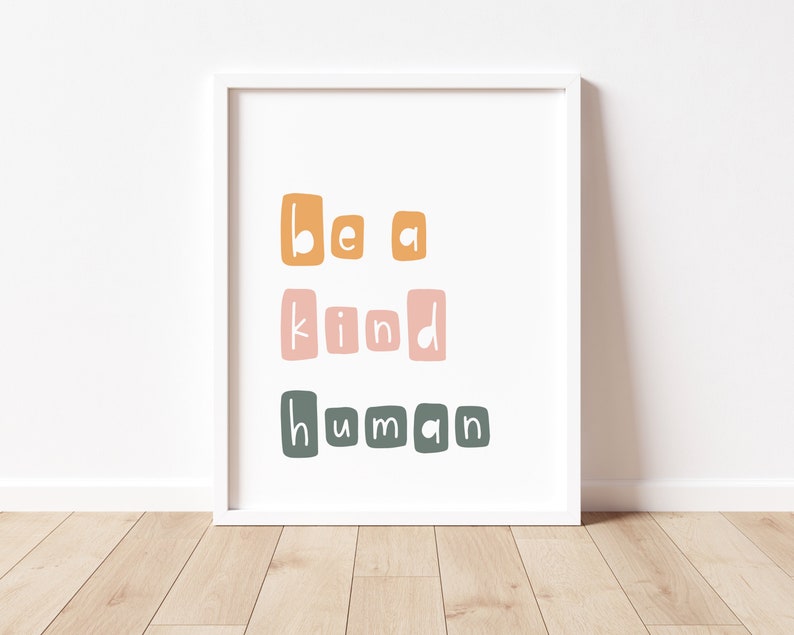 Puede incluir: Una impresi&oacute;n art&iacute;stica enmarcada con la frase "be a kind human" en una fuente l&uacute;dica y en bloques. El texto est&aacute; dispuesto en tres l&iacute;neas, con cada palabra en un color diferente: naranja, rosa y verde. La impresi&oacute;n est&aacute; sobre un fondo blanco.