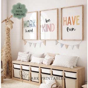 Può includere: Tre stampe incorniciate con le frasi "WORK hard", "be KIND" e "HAVE fun" in lettere colorate. Sotto le stampe c'è un mobile contenitore in legno con contenitori bianchi. Una giraffa decorativa e cuscini completano l'arredamento della stanza.