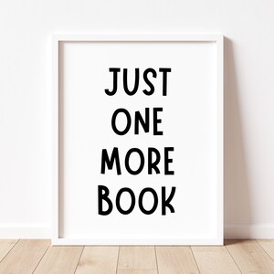 May include: White framed print with black text that reads "JUST ONE MORE BOOK" on a white wall.