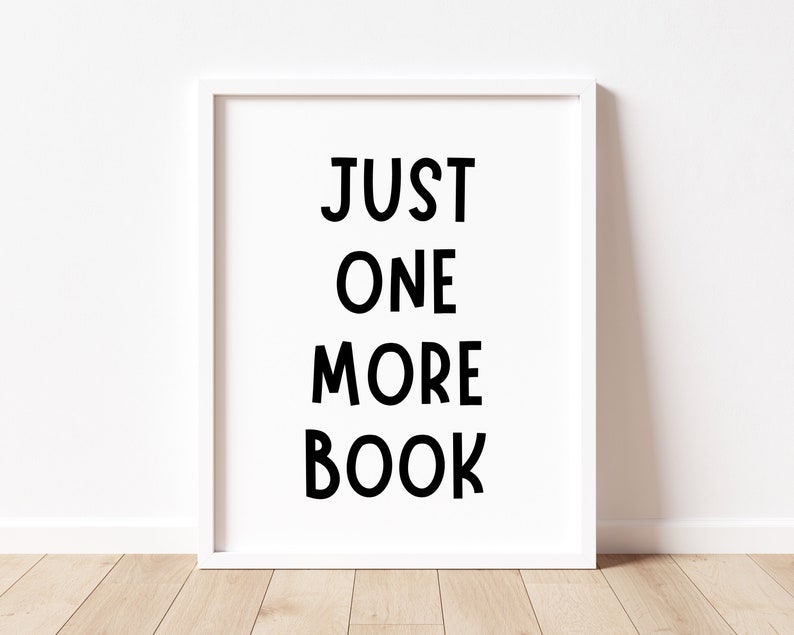 May include: White framed print with black text that reads "JUST ONE MORE BOOK" on a white wall.