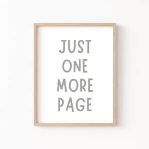 May include: A framed print with the text "JUST ONE MORE PAGE" in gray lettering on a white background. The frame is light wood.