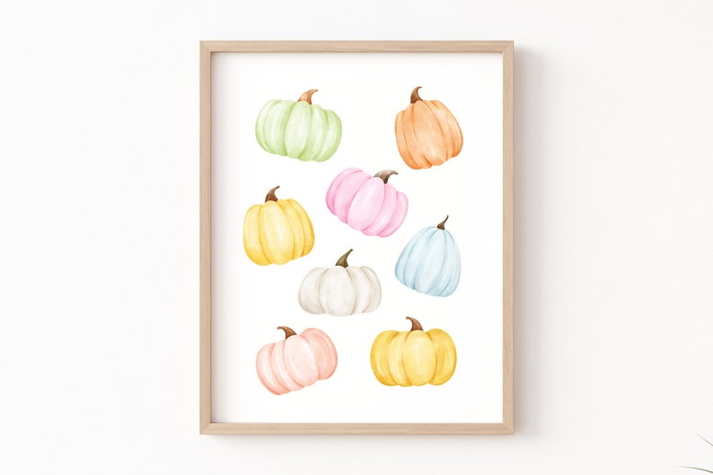 May include: A framed print featuring nine watercolor pumpkins in various pastel colors, including light green, orange, pink, yellow, white, and blue. The pumpkins are arranged in a random pattern on a white background.