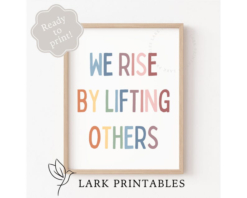 May include: A framed print with the text "WE RISE BY LIFTING OTHERS" in colorful, playful lettering. The print is in a light wood frame and includes the text "Ready to print!" and "LARK PRINTABLES".