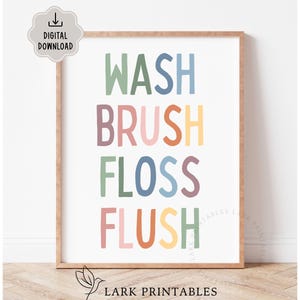 Könnte beinhalten: Ein gerahmter Druck mit den Worten "WASH BRUSH FLOSS FLUSH" in farbenfrohen, verspielten Buchstaben. Der Text ist vertikal auf weißem Hintergrund angeordnet, mit einem hellbraunen Rahmen. Das Bild enthält auch ein "DIGITAL DOWNLOAD"-Symbol.