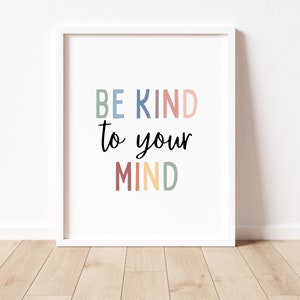 Op de afbeelding: Witte ingelijste print met de tekst "BE KIND to your MIND" in kleurrijke letters. De letters zijn in tinten blauw, roze, rood, geel en groen.