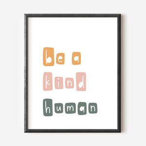 Puede incluir: Una impresi&oacute;n art&iacute;stica enmarcada con la frase "be a kind human" en un estilo de letras de bloque. El texto est&aacute; dispuesto en tres l&iacute;neas, con cada palabra en un color diferente: naranja, rosa y verde. La impresi&oacute;n est&aacute; sobre un fondo blanco.