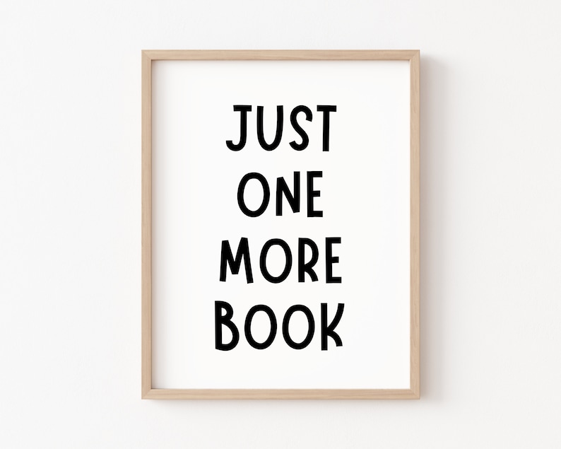May include: A framed print with the text "JUST ONE MORE BOOK" in black bold letters on a white background.
