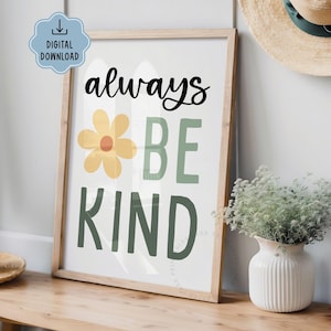 May include: A framed print with the words "always BE KIND" in black and green. A yellow flower graphic is between "always" and "BE". The print is in a light wood frame and is on a wooden surface.