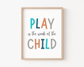 May include: A framed print with the text "PLAY is the work of the CHILD" in colorful letters. The letters are in shades of blue, orange, and gray. The background is white.