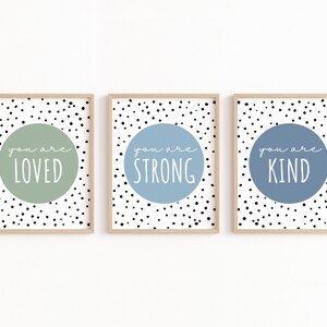 May include: Three framed prints with black and white polka dot backgrounds. Each print features a light blue or green circle with white text that reads "you are loved", "you are strong", and "you are kind".