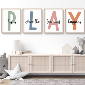 Può includere: Quattro stampe incorniciate con la parola "PLAY" scritta in grandi lettere colorate. Le lettere sono di colori diversi: verde, blu, rosa e arancione. Il testo "This is where the learning happens" è scritto in nero sotto le lettere.