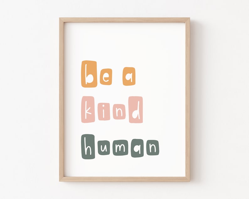 Puede incluir: Impresi&oacute;n enmarcada con la frase "Be a kind human" en una fuente l&uacute;dica y en bloques. El texto est&aacute; dispuesto en tres l&iacute;neas, con las palabras en naranja, rosa y verde. El marco es de color madera clara.