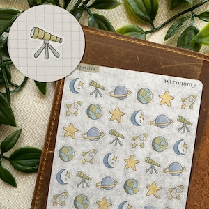 May include: A sheet of astronomy-themed stickers featuring illustrations of telescopes, planets, stars, rockets, and crescent moons. The word "astronomy" is printed on the sheet. A separate sticker shows a telescope on a tripod. The word "petites" is printed on the sheet.